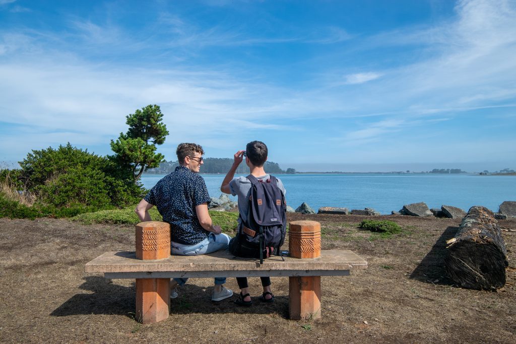Two people sitting on a park bench overlooking the water
