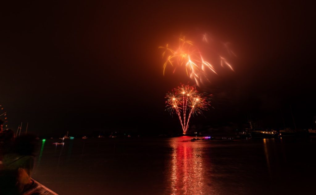 Red and orange fireworks going off over water at night