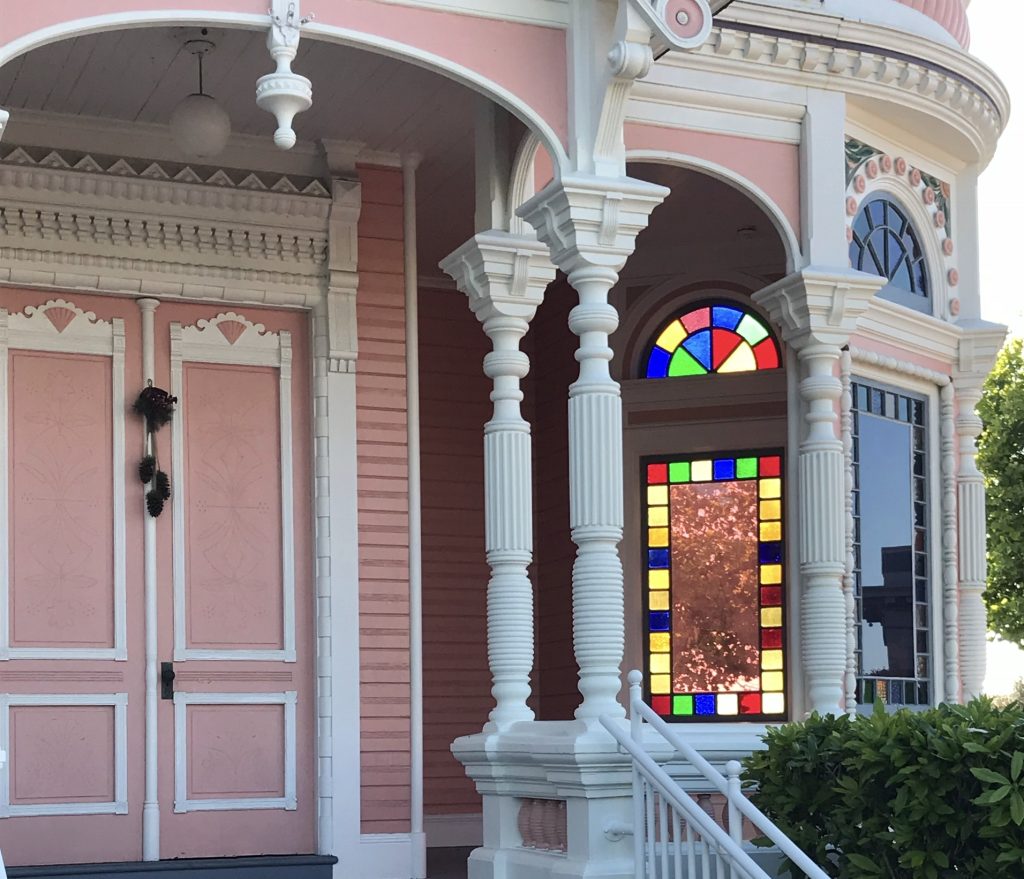 Pink exterior of victorian style house with rainbow color stain glass windows