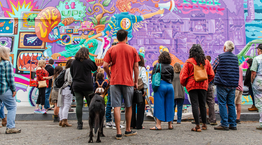 People looking at and observing a colorful mural on the side of a building
