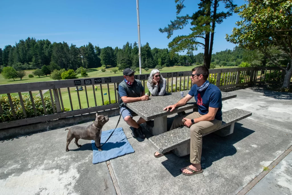 group of of people sitting at a picnic bench with a dog by a golf course