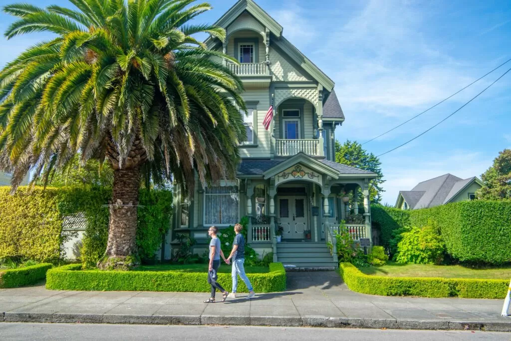 Couple walking past a green Victorian house with a big palms tree